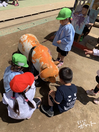 園庭に置かれた、パンダの遊具に絵の具を塗る子どもたちの写真。